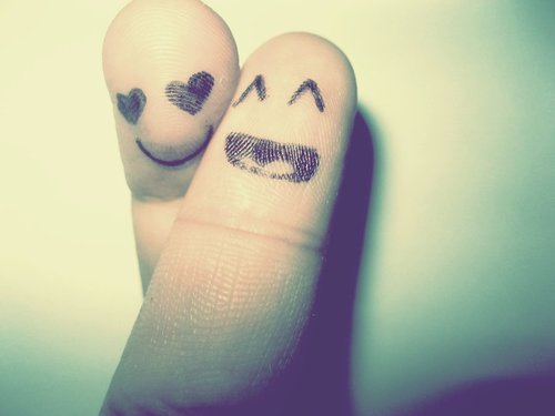 Two crossed fingers with happy and loving faces drawn on htem